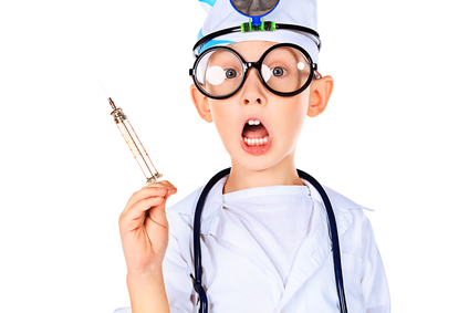 Portrait of a funny boy in big spectacles playing doctor with syringe and a stethoscope. Isolated over white.